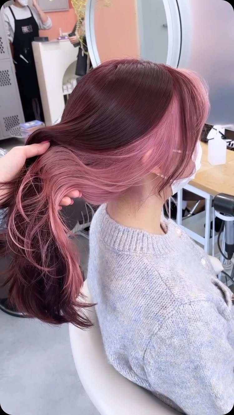 Dusty pink hair styled in long waves with a dark plum section in a salon