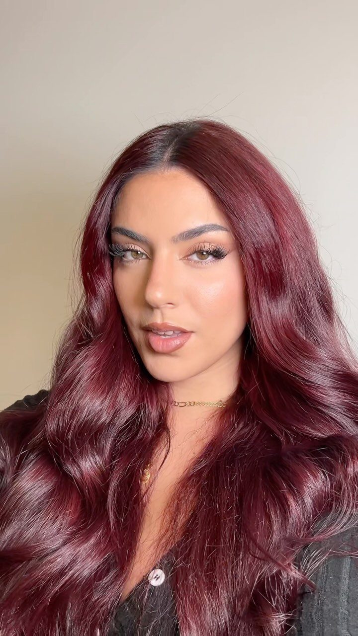 Woman with long, glossy burgundy-red hair against a plain beige wall