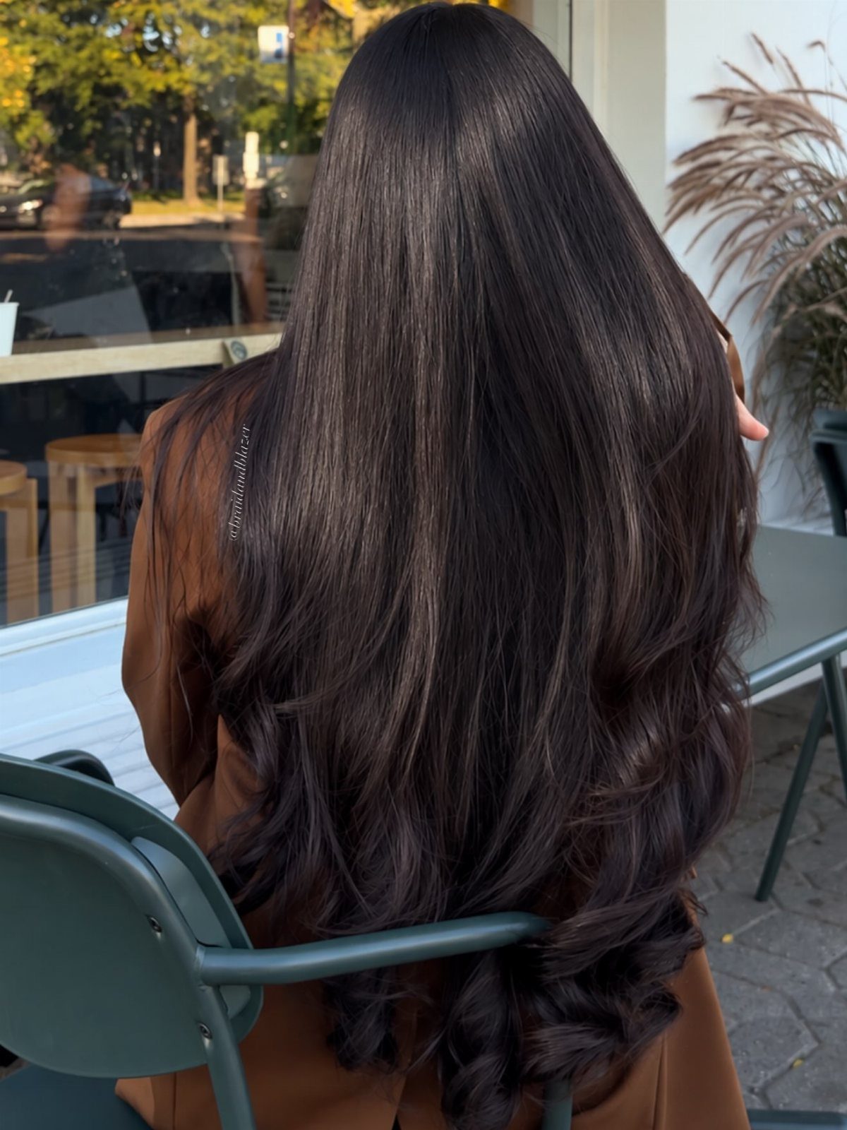 Long soft-black hair falls down a seated person's back in loose curls