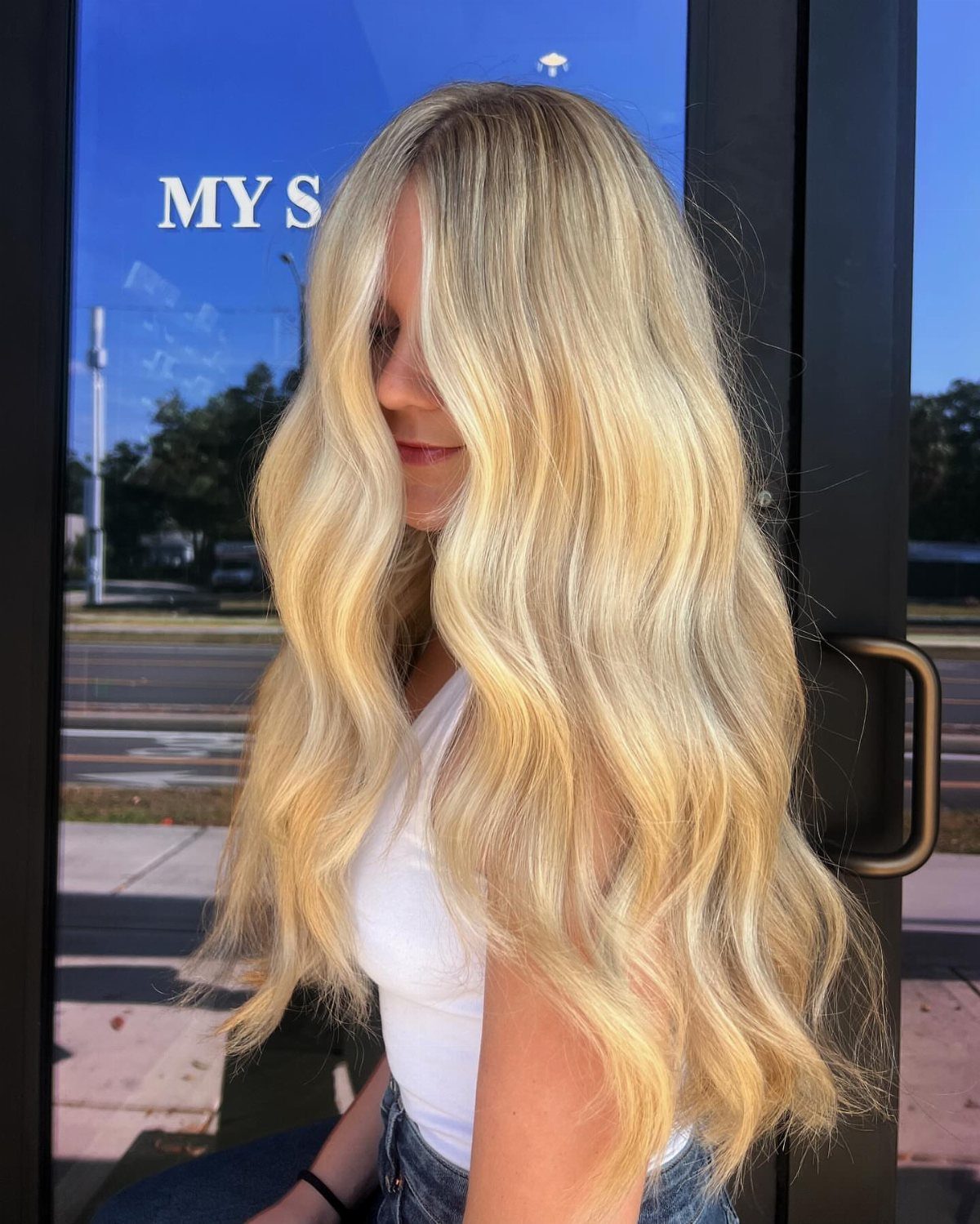 Long blonde hair with sunlit highlights falls in loose waves over a white top