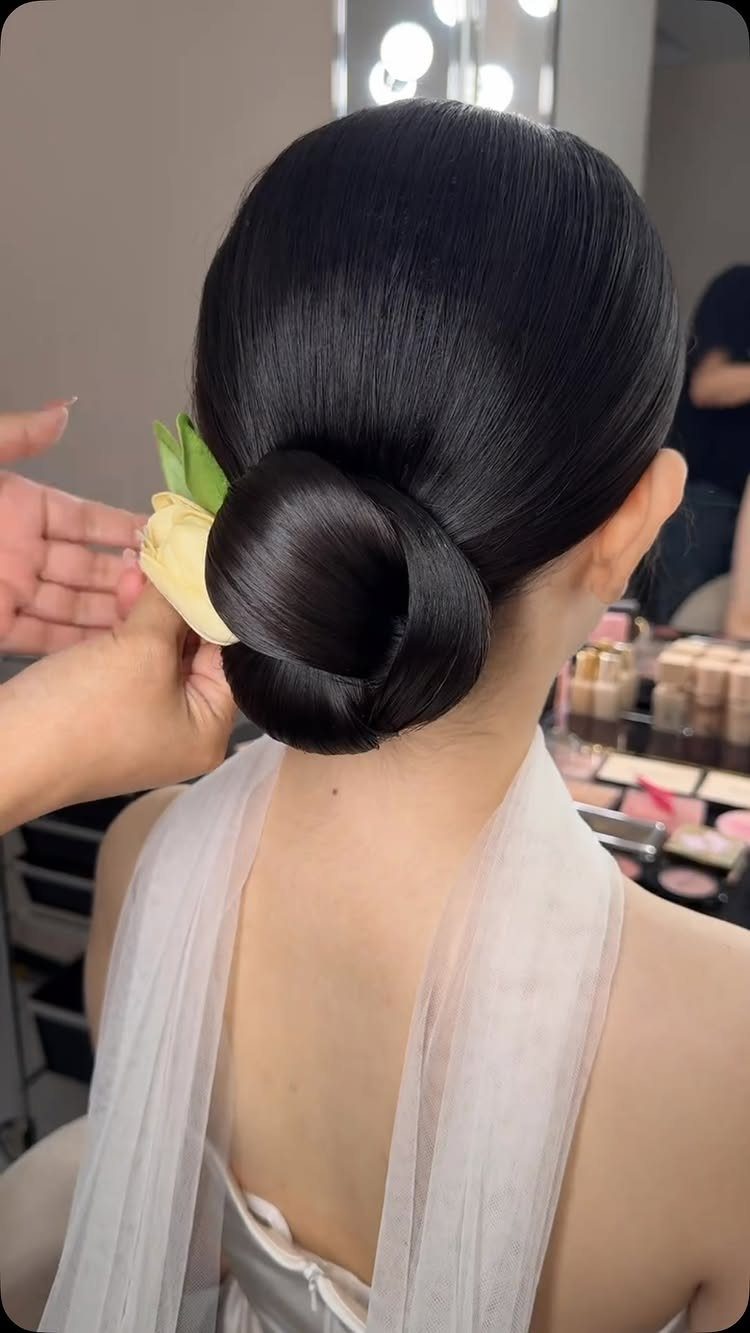 Sleek low chignon with a cream flower on a woman in a white dress