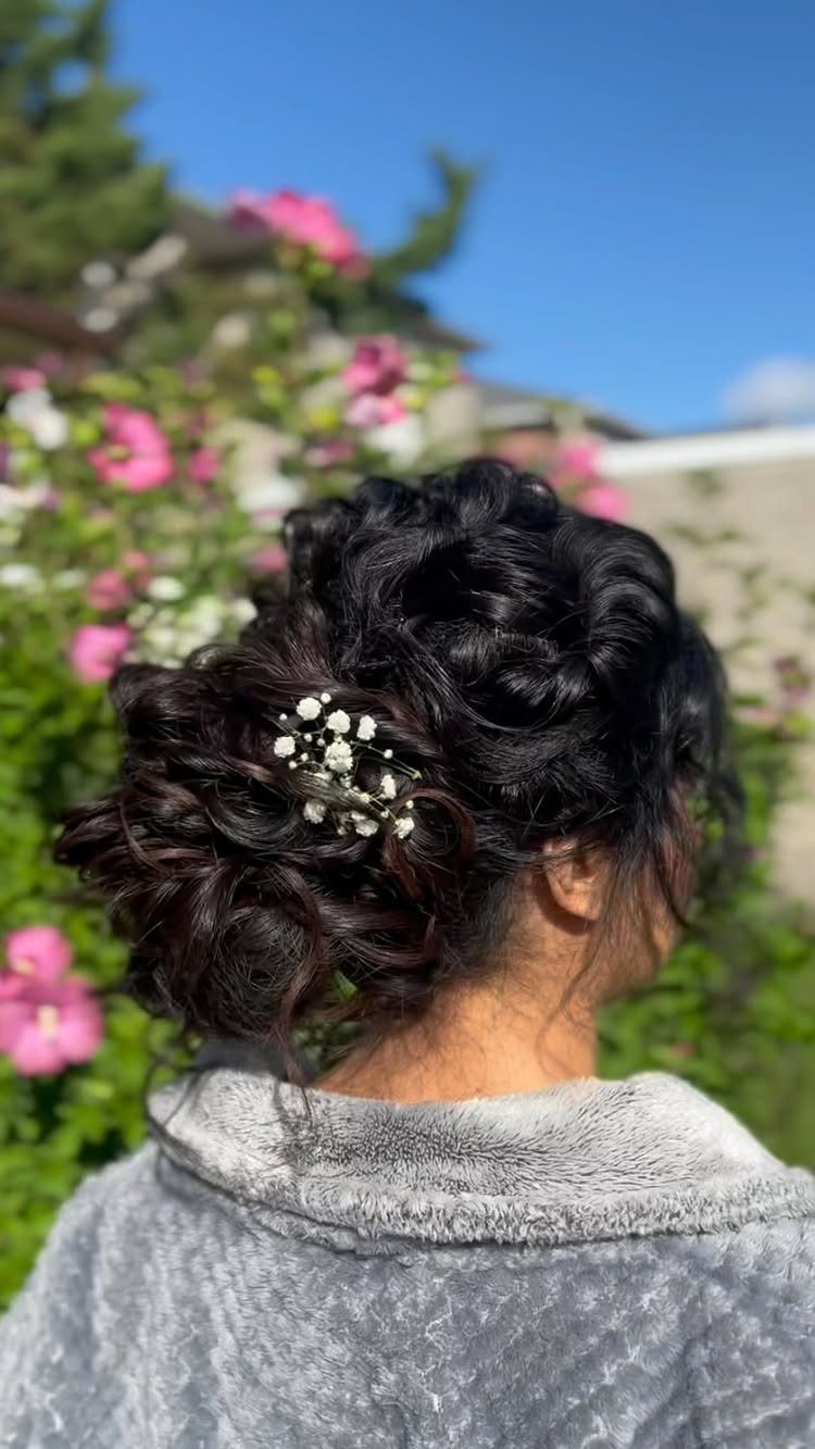 Curly updo with small white floral pins against a garden backdrop