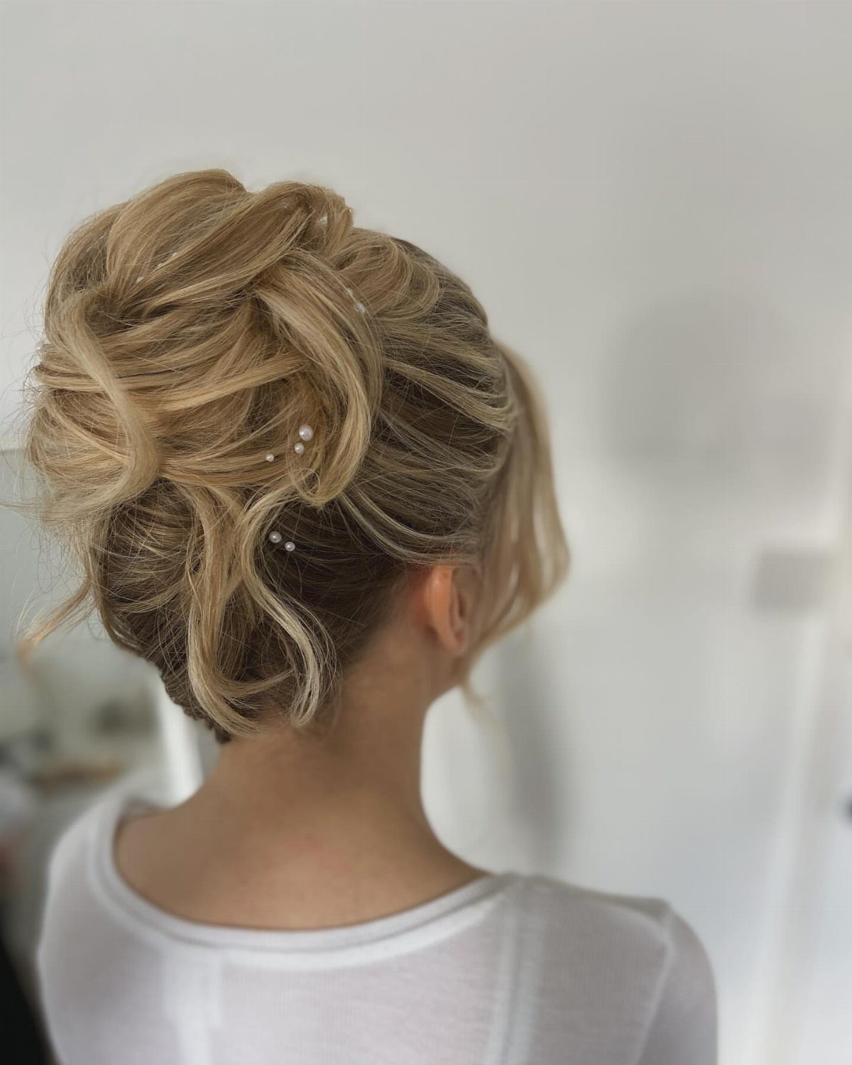 Blonde curled updo decorated with pearl pins, viewed from behind