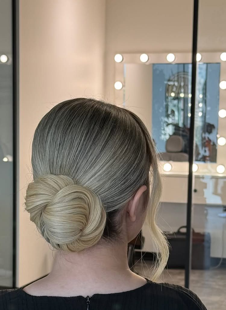 Sleek blonde low updo with a sculpted bun and loose face-framing curl