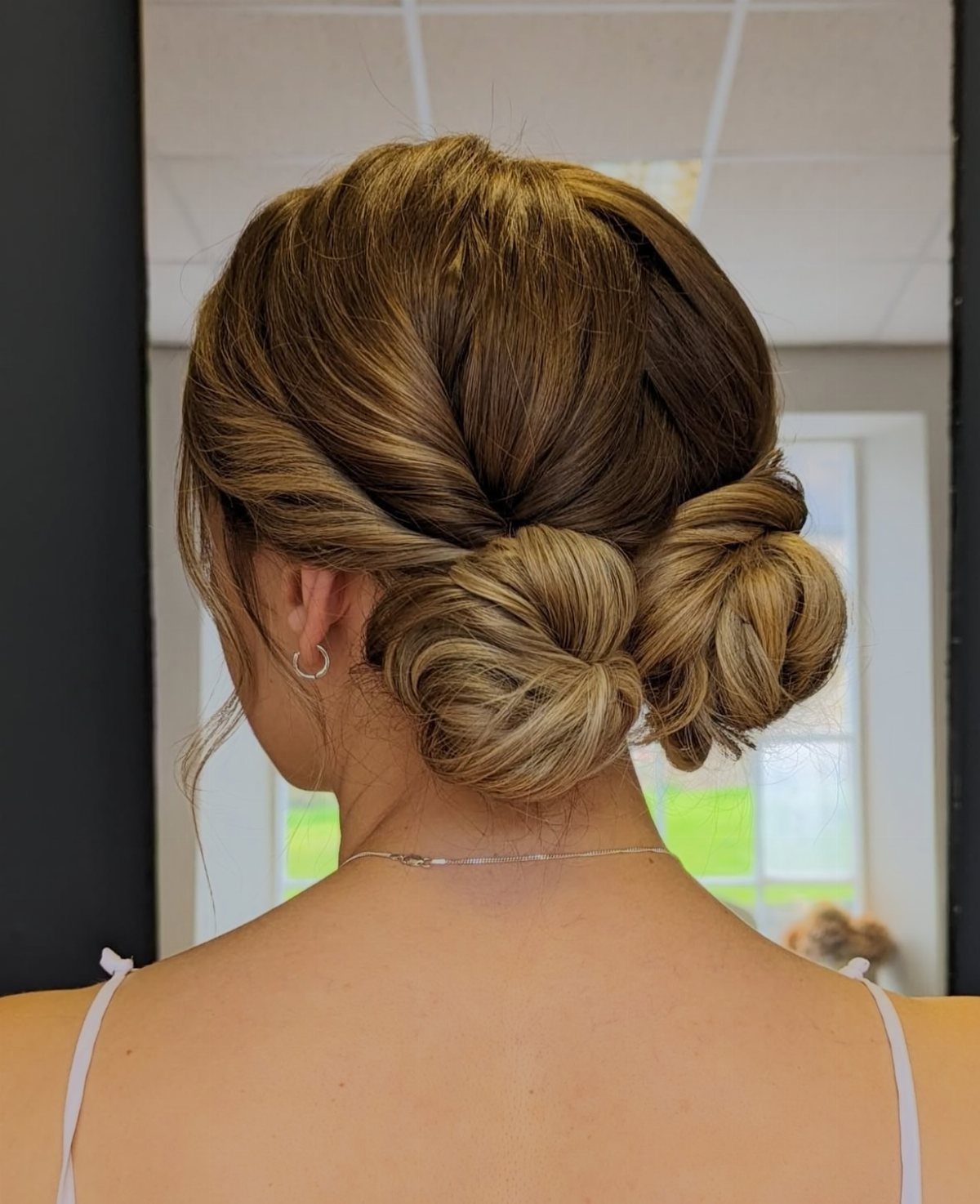 Two twisted low buns secure a woman's brown hair at the nape.