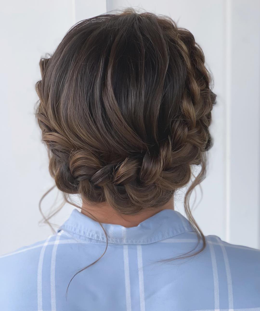 Braided updo wraps around the head with curled tendrils and loose strands