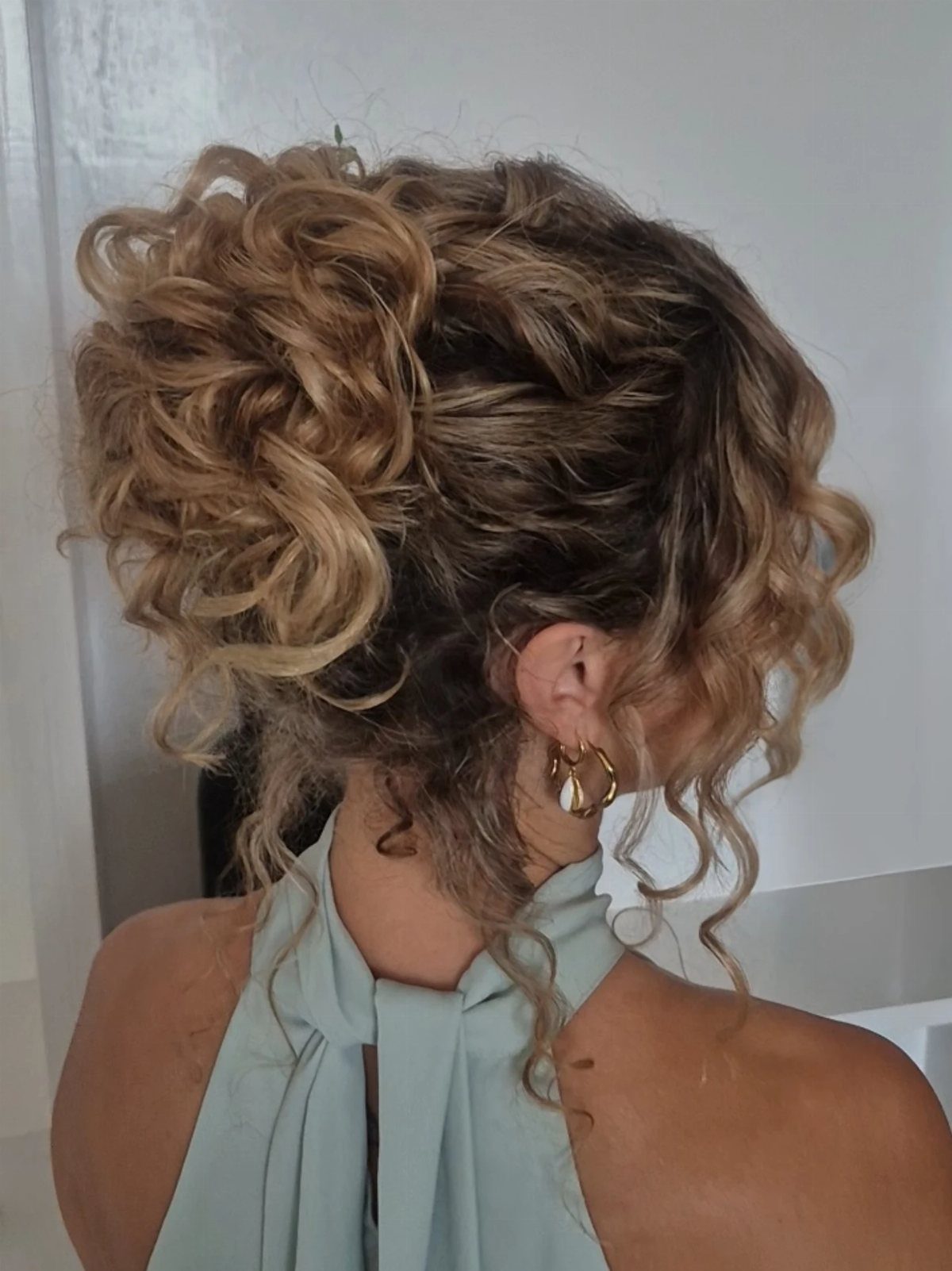 Woman with a voluminous curly updo and loose tendrils framing her face