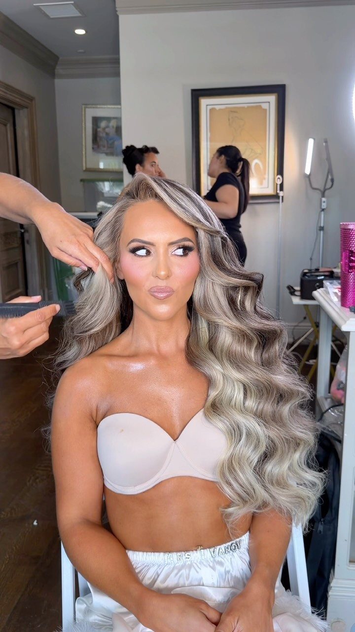 Woman with long, glossy silver-blonde Hollywood waves seated while a stylist works