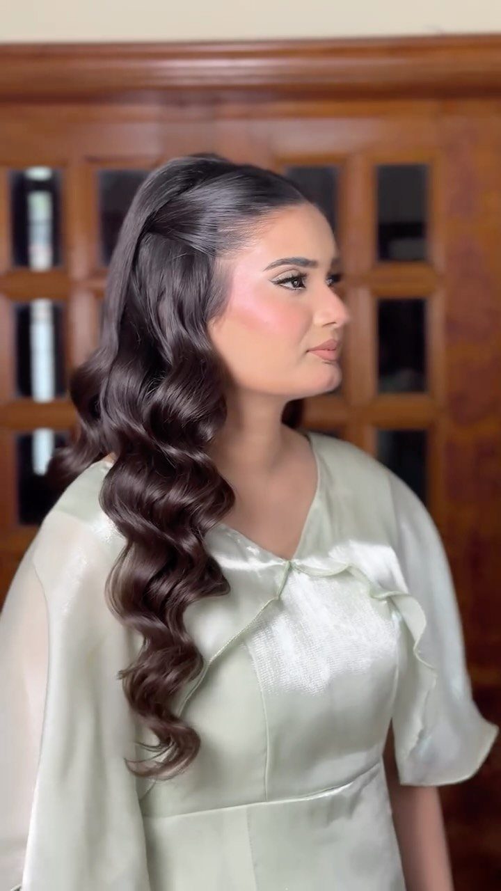 Woman with long dark hair styled in glossy loose waves, pinned back at the front