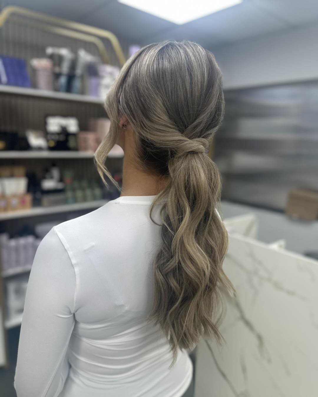 Long wavy ash-blonde hair gathered into a wrapped low ponytail