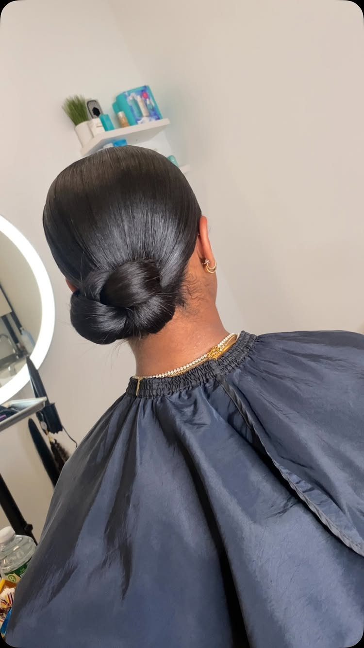 Glossy black hair styled into a smooth, polished low bun at the nape