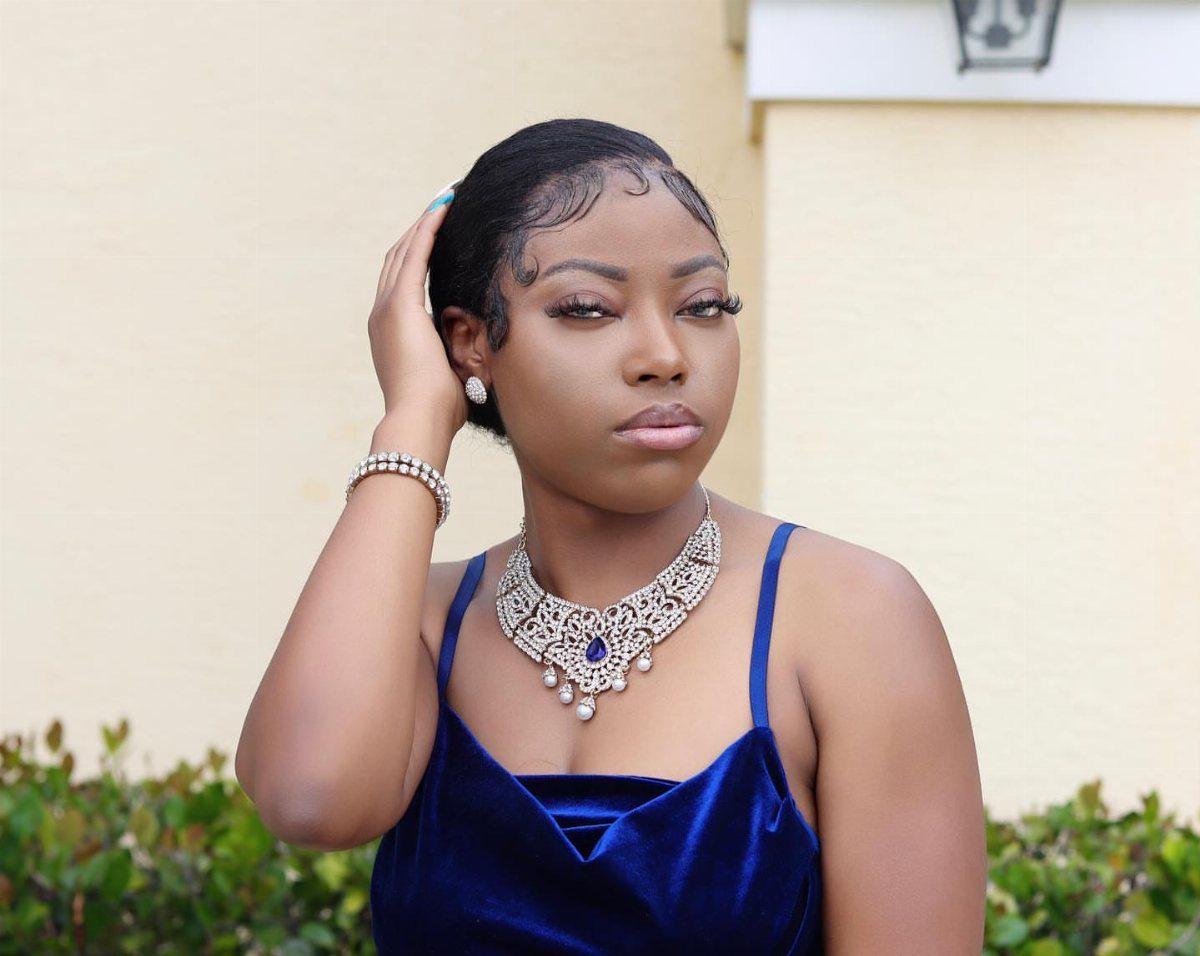 Woman wearing slicked-back short hair, a blue velvet dress, and jeweled necklace outdoors