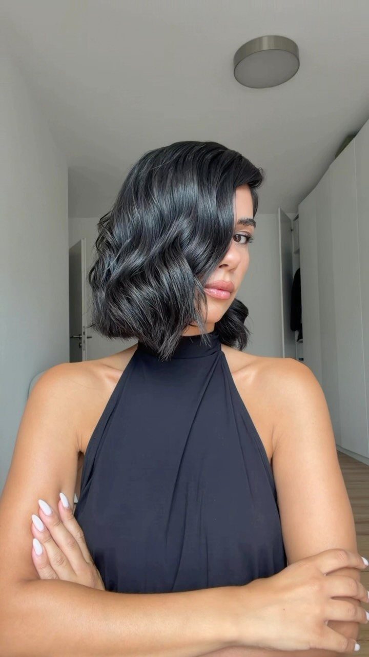 Woman posing with a glossy, shoulder-length wavy bob and side part