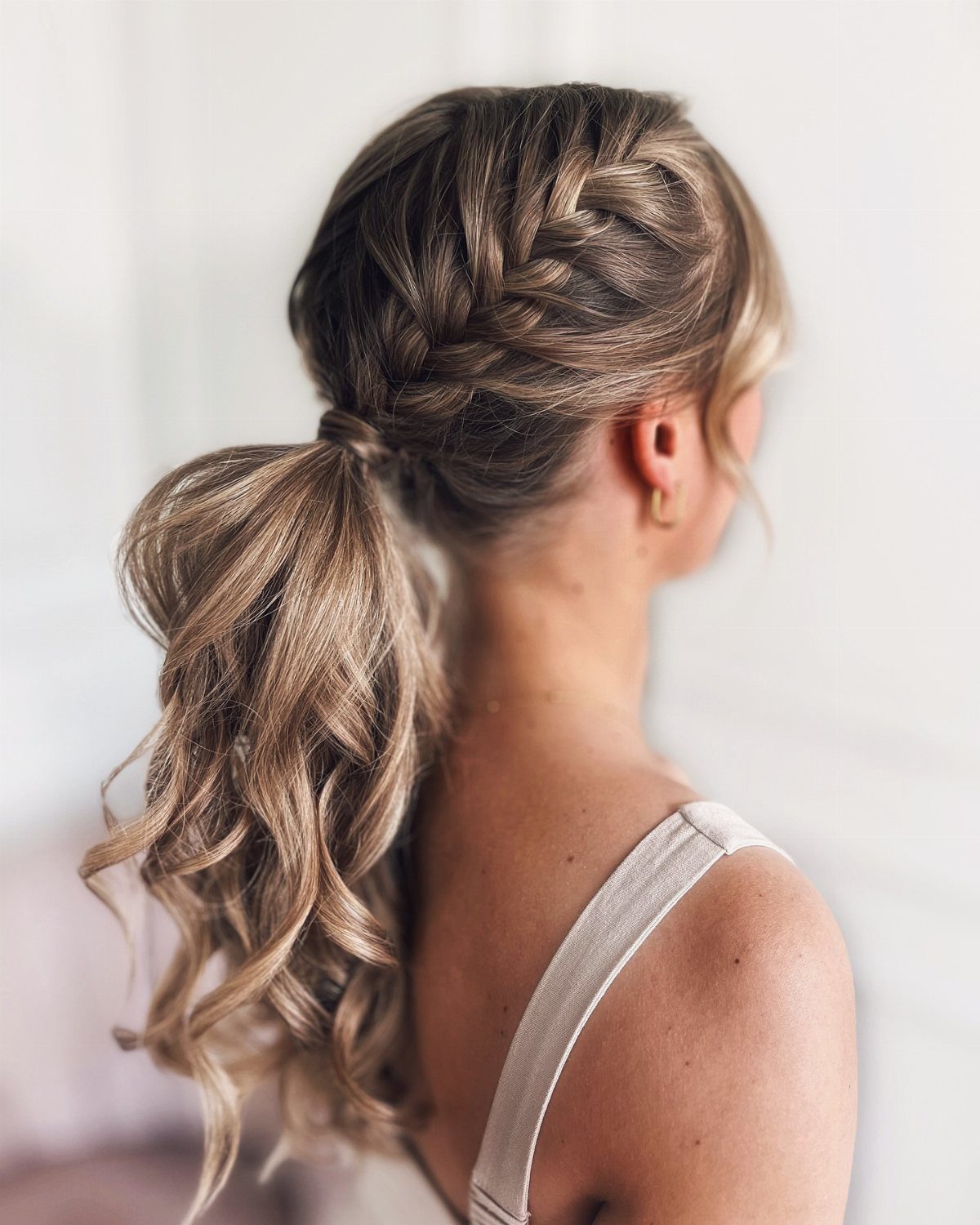Braided low ponytail with curled lengths on a woman viewed from behind
