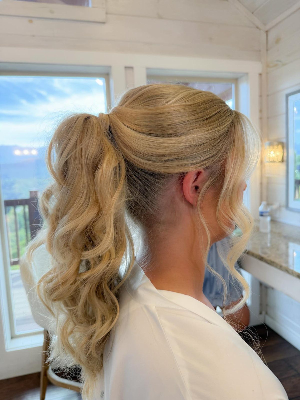 Blonde wedding updo with a voluminous curled ponytail cascading down