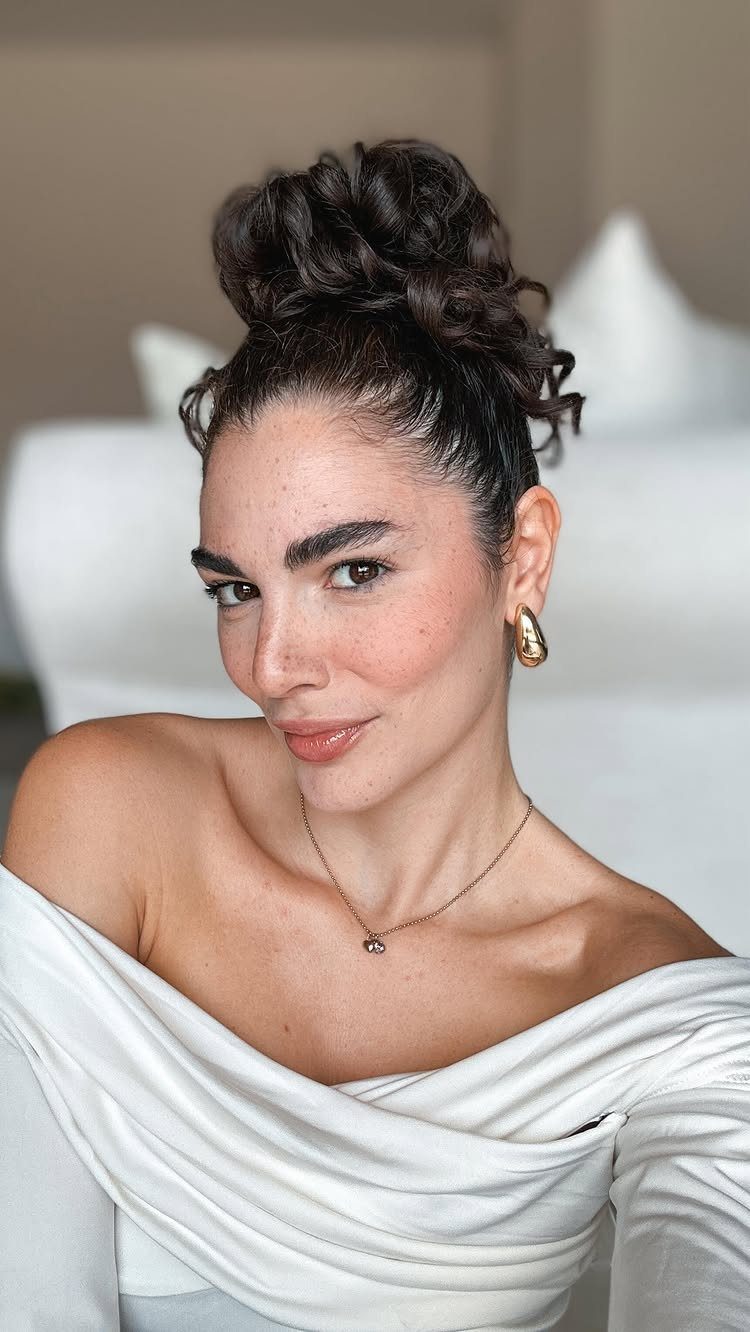 Woman wearing a voluminous curly updo with loose tendrils and gold earrings