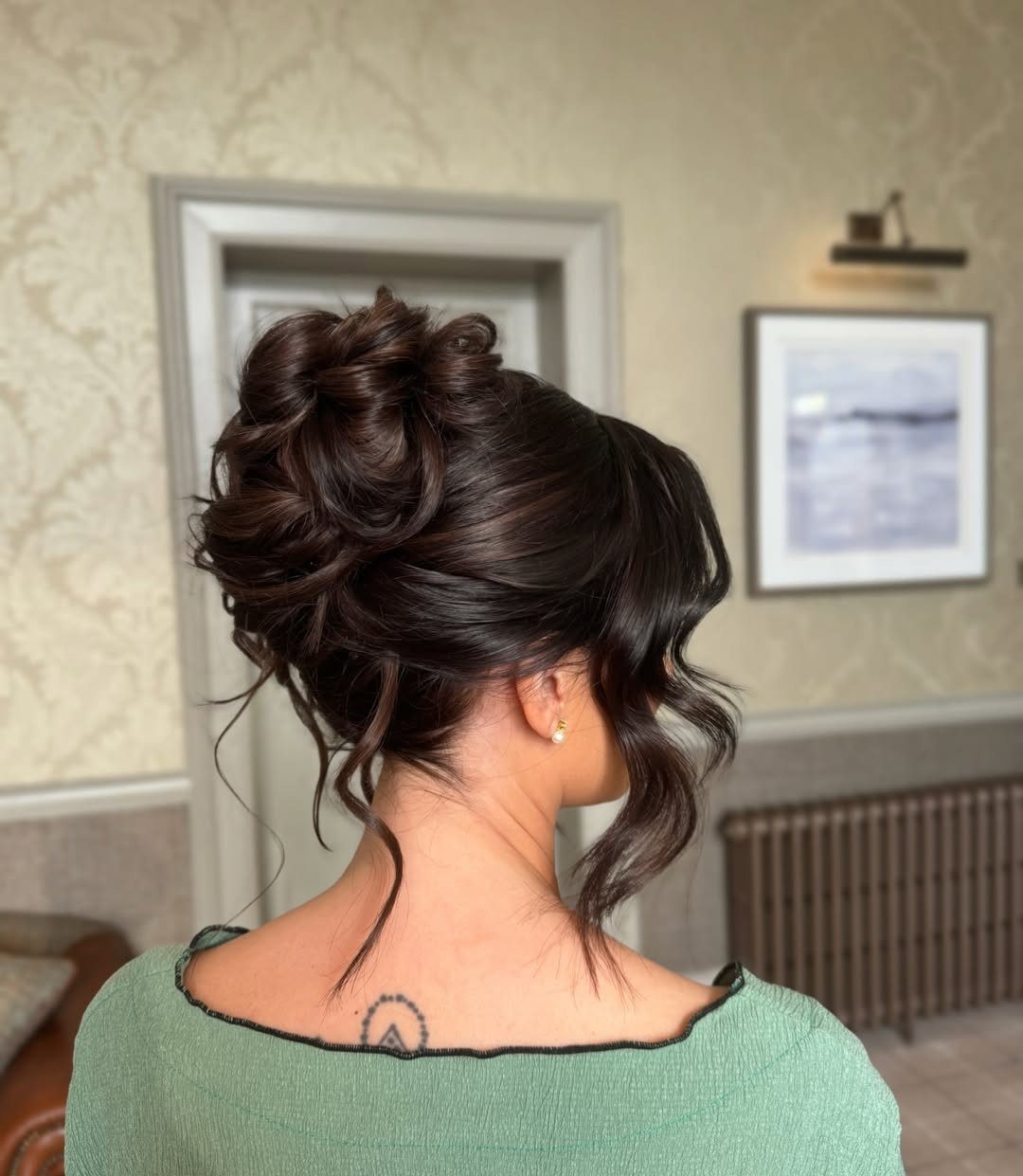 Woman wearing a voluminous high top knot with loose curls and face-framing tendrils
