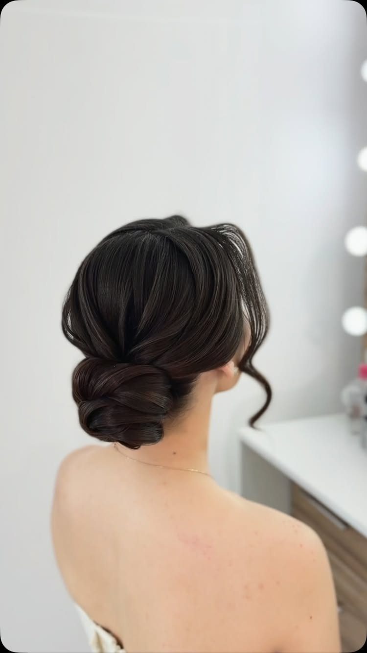 Dark-haired woman wearing a sculpted low updo with a loose curl