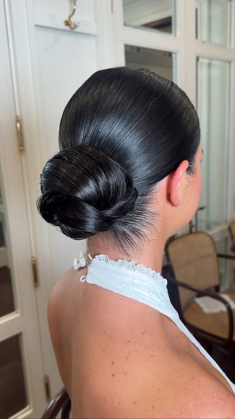 Woman with glossy slicked-back hair gathered into a low bun