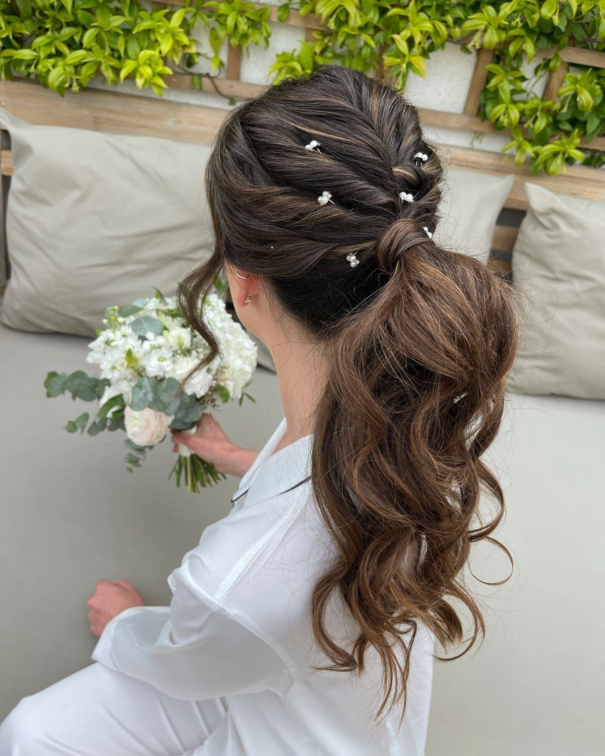 Long brown bridal ponytail styled in waves with delicate white hair ornaments