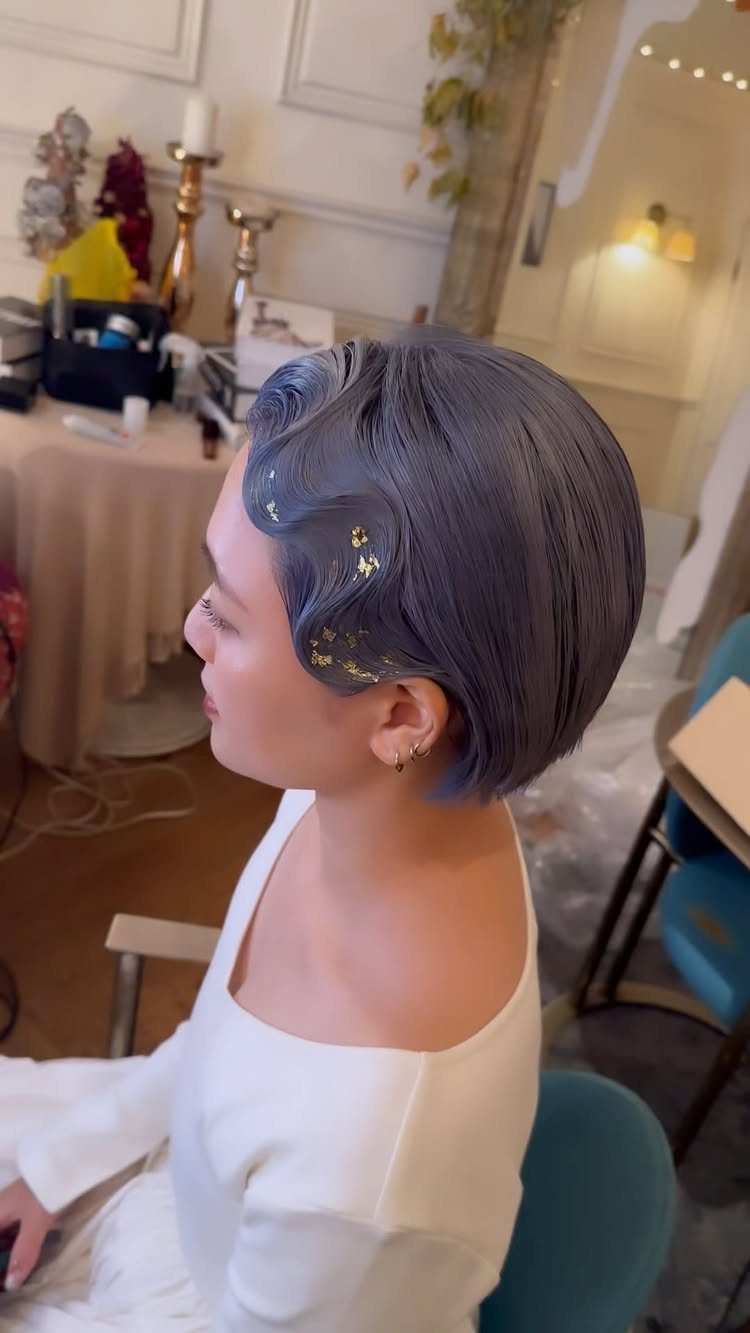 Woman with short dark hair in sculpted S-shaped waves and gold accents