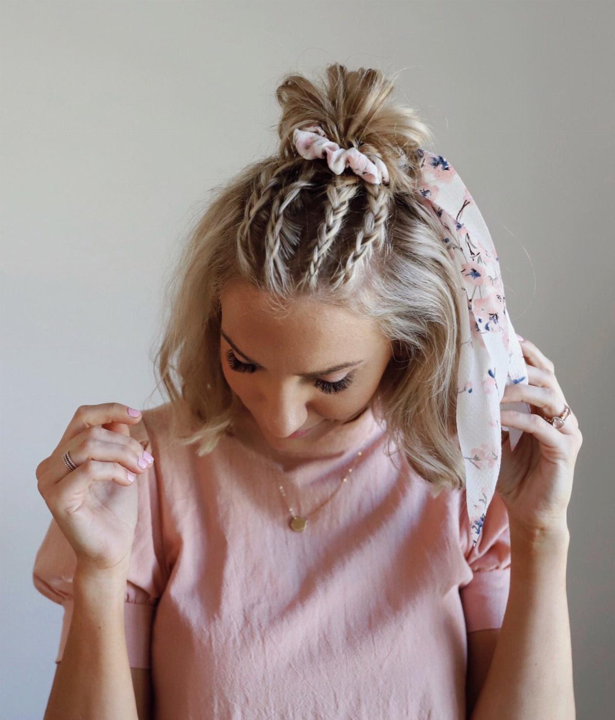 Braided blonde hair gathered into a small scrunchie topknot with loose lengths