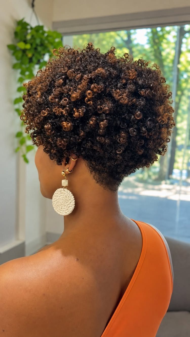 Short natural curls with brown highlights frame the back of the wearer’s head
