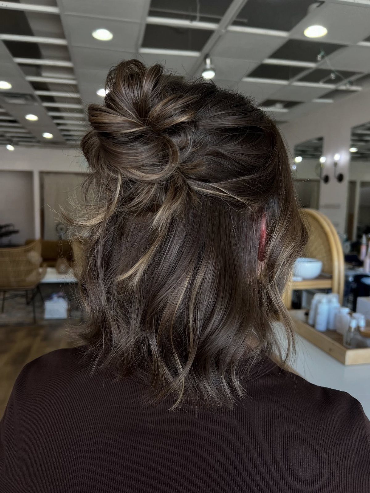 Dark wavy hair styled in a loose twisted half-up bun at a salon